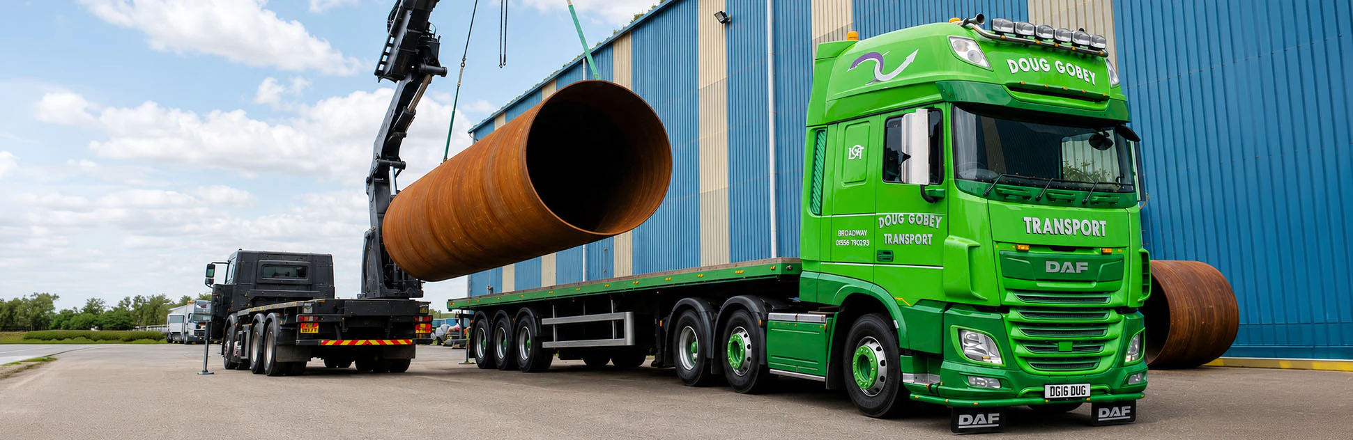 Doug Gobey crane lorry lifting a large steel pipe beside a warehouse
