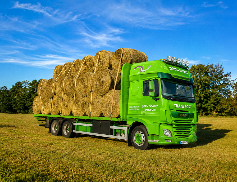 Doug Gobey flatbed lorry loaded with round hay bales in a field