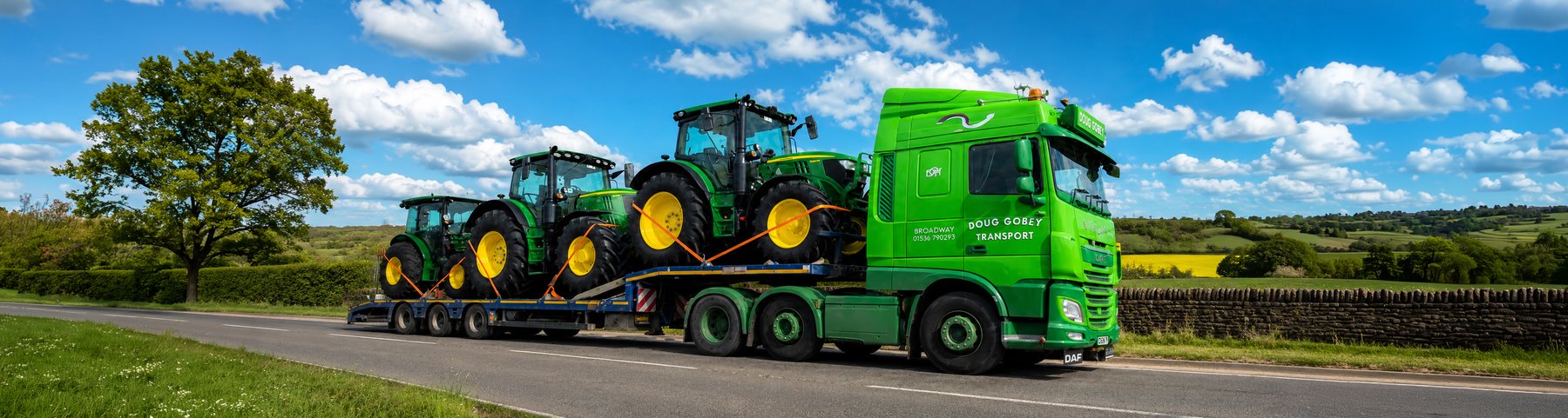 Doug Gobey lorry carrying two green tractors on a low-loader along a country road